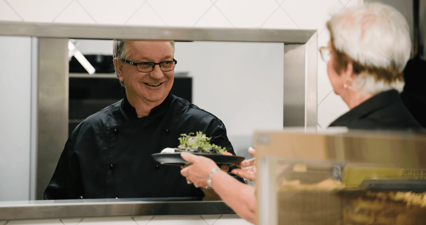 Chef handing food over to a waitress through the kitchen pass