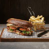 A pretzel BLT on a wooden board with a basket of fries