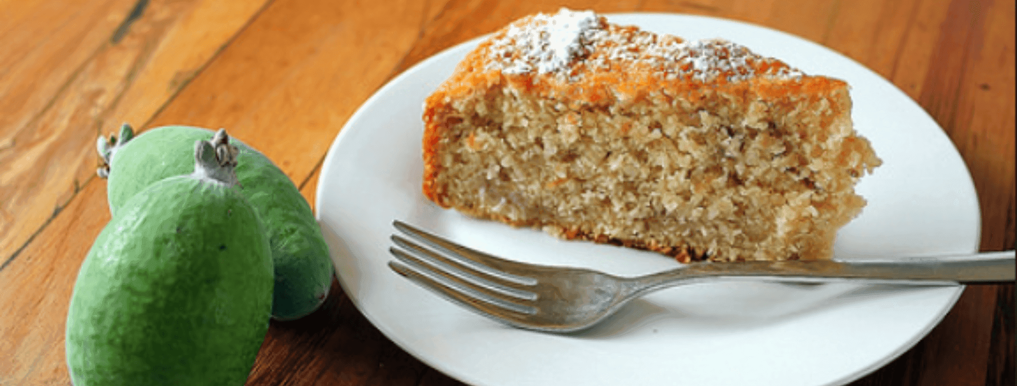 Slice of cake on a white plate with a fork. Feijoas next to the plate