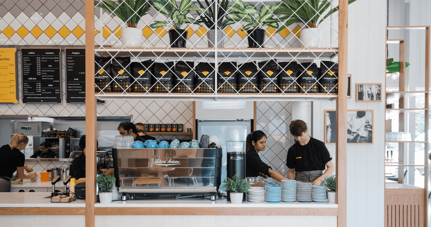 Two staff members next to a coffee machine behind a cafe counter
